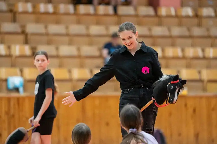 Ukázka Hobby Horsing ve sportovní hale se ženou držící černého Hobby Horse