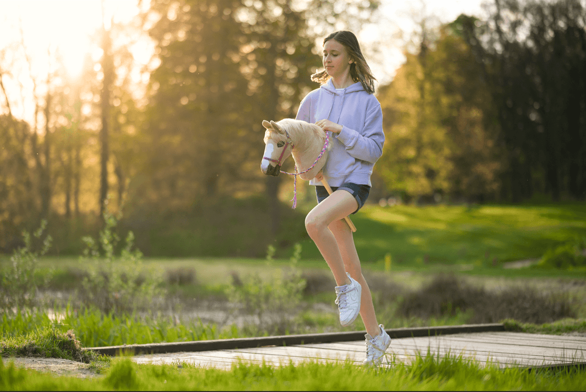 Dívka si užívá Hobby Horsing venku s bílým Hobby Horse při západu slunce