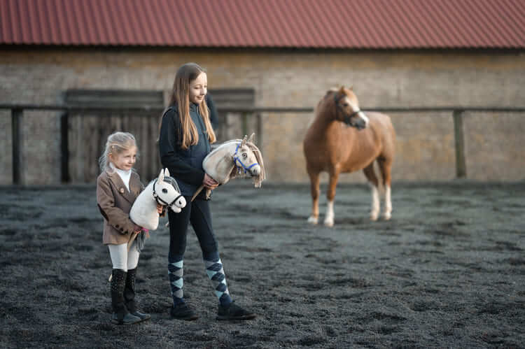 Dvě děti nesou Hobby Horses na venkovním kolbišti vedle poníka