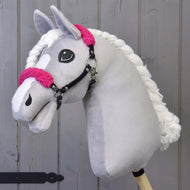 Černá ohlávka z koženky s růžovým beránkem od Hobby Horse LarDen na světle šedé plyšové hlavě, s růžovými beránkovými detaily, bílou přízovou hřívou a černou ohlávkou na dřevěné tyči, na pozadí z dřevěných prken.