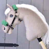 Hračka Hobby Horse LarDen s béžovou plyšovou hlavou, bílou přízovou hřívou a černou ohlávkou se zeleným beránkem z koženky na šedo-dřevěném pozadí.