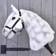 Hobby Horse Elektra s černou ohlávkou od Hobby Horse LarDen s plyšovým bílým provedením, modrýma očima a černou ohlávkou, nasazený na tyči před šedou dřevěnou stěnou.