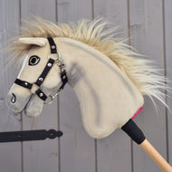 Hobby Horse Ivory Dream s černou ohlávkou – velikost XS od Hobby Horse LarDen, s jemnou krémovou srstí a dřevěnou tyčí, opřené o šedou dřevěnou stěnu.