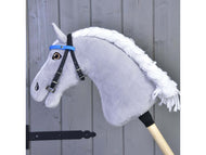 Uzdečka s čelenkou bez nánosníku modrá (vel. S) od Hobby Horse LarDen na šedém Hobby Horse s bílou přízovou hřívou, nasazeném na dřevěné tyči před šedými dřevěnými dveřmi.