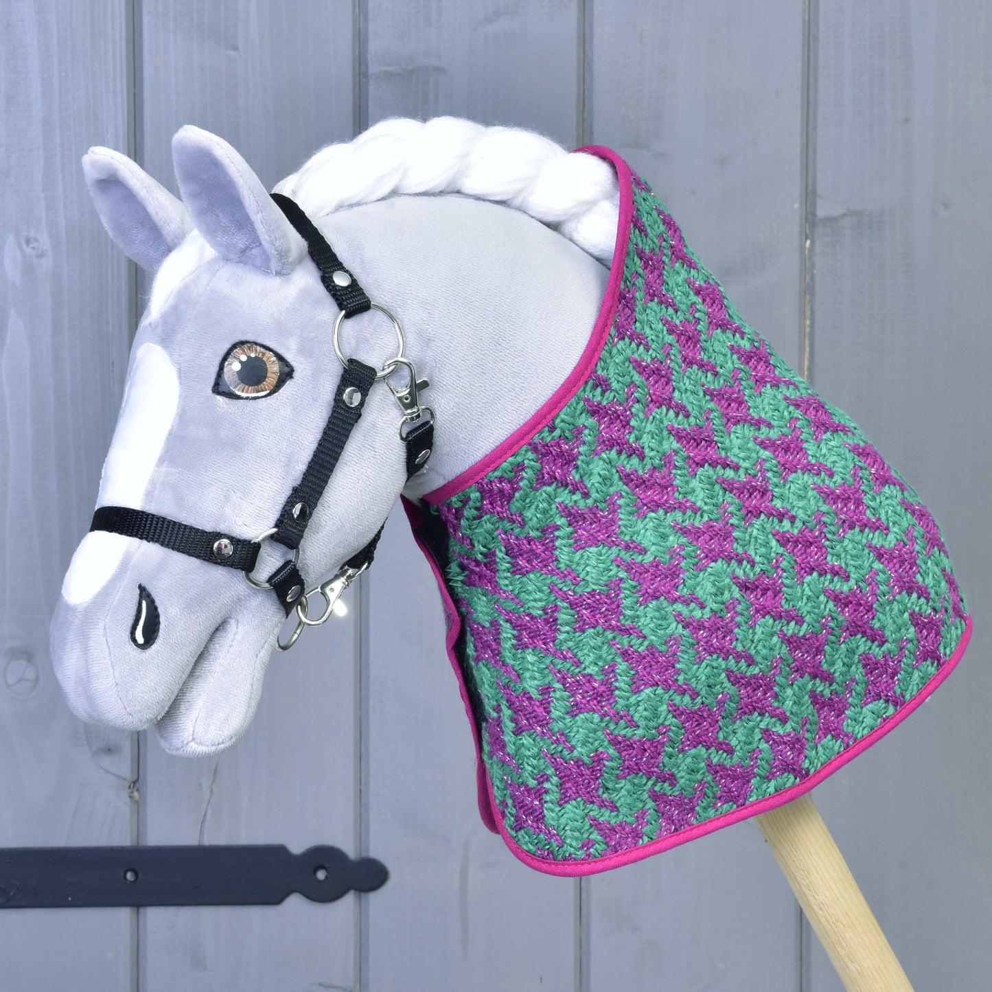 Set Coco od Hobby Horse LarDen: šedý Hobby Horse s černou uzdečkou, ve fialovo-zeleném setu deky se vzorem kohoutí stopy, růžovým lemem a čabrakou na uši, před šedou dřevěnou stěnou.