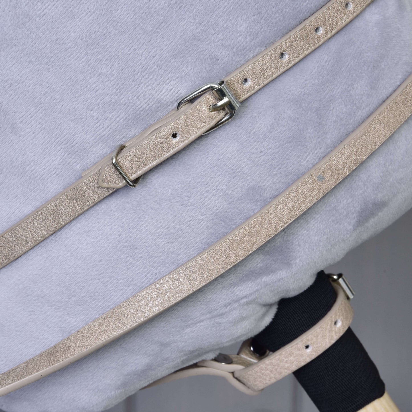 Detail béžových řemínků z koženky Bordeaux s kovovými přezkami ze setu uzdečky, otěží a martingalu od Hobby Horse LarDen, upevněných přes měkký světle šedý plyšový povrch.