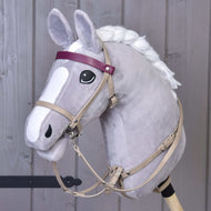 Šedý plyšový Hobby Horse od Hobby Horse LarDen s koženkovým setem Bordeaux – uzdečka, otěže a martingal –, bílou hřívou, černo-bílýma očima a fialovou čelenkou stojí před dřevěným pozadím.