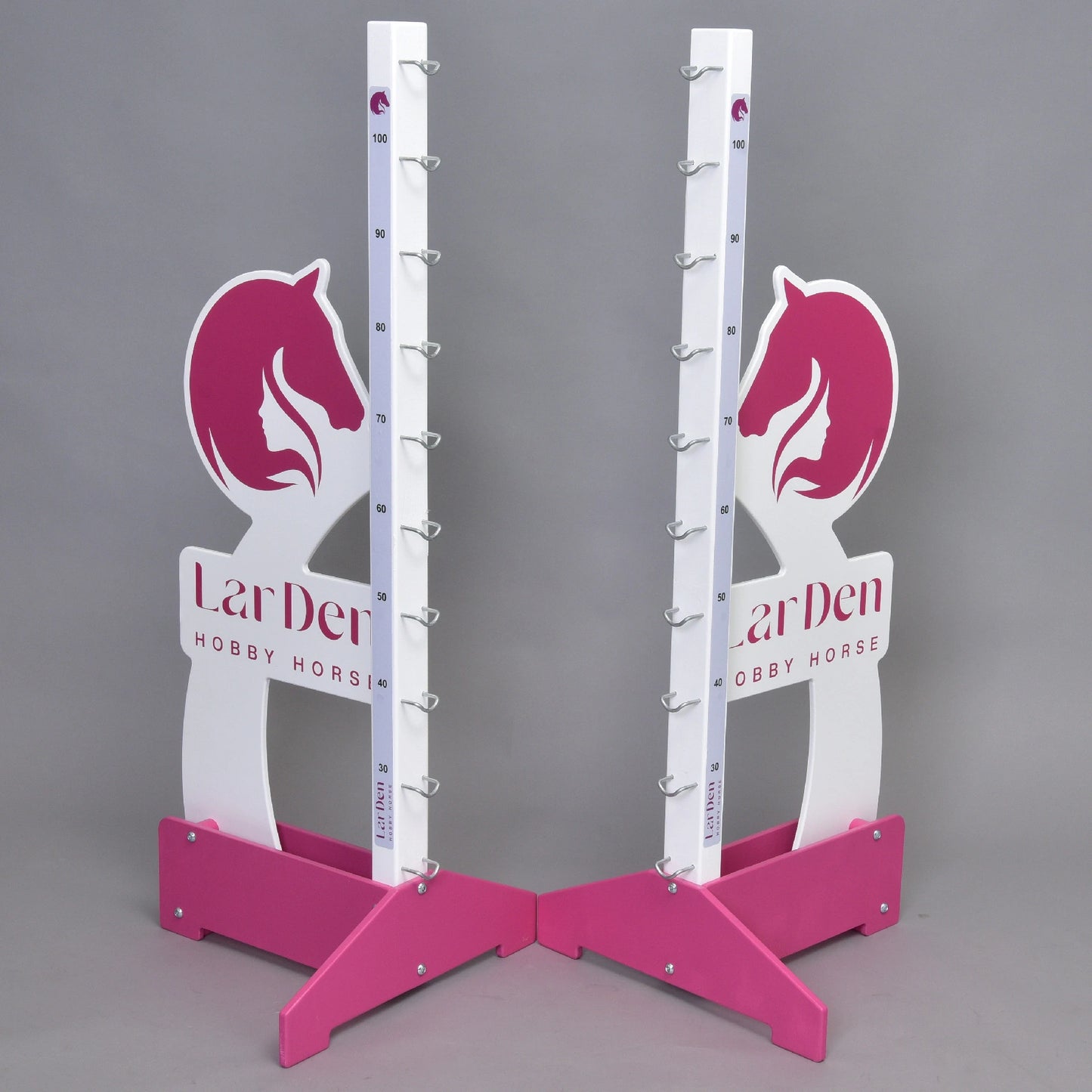 Dva stojany Překážka LarDen kolmák 110 cm od Hobby Horse LarDen v růžové a bílé barvě s motivy koňských hlav, značkami nastavitelné výšky a kovovými držáky na tyče stojí na šedém pozadí. Na základně je vytištěno „LarDen HOBBY HORSE“.