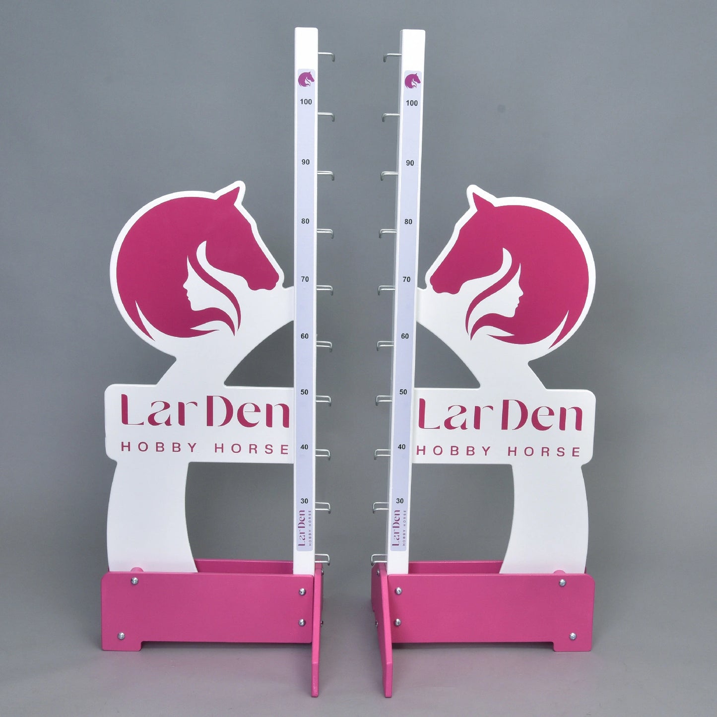 Dva bílé a růžové stojany Překážka LarDen kolmák 110 cm od Hobby Horse LarDen s nastavitelnou výškou až do 110 cm, grafikou koňské hlavy a textem značky na základně — ideální pro jízdu na Hobby Horse, zobrazeno na jednobarevném šedém pozadí.