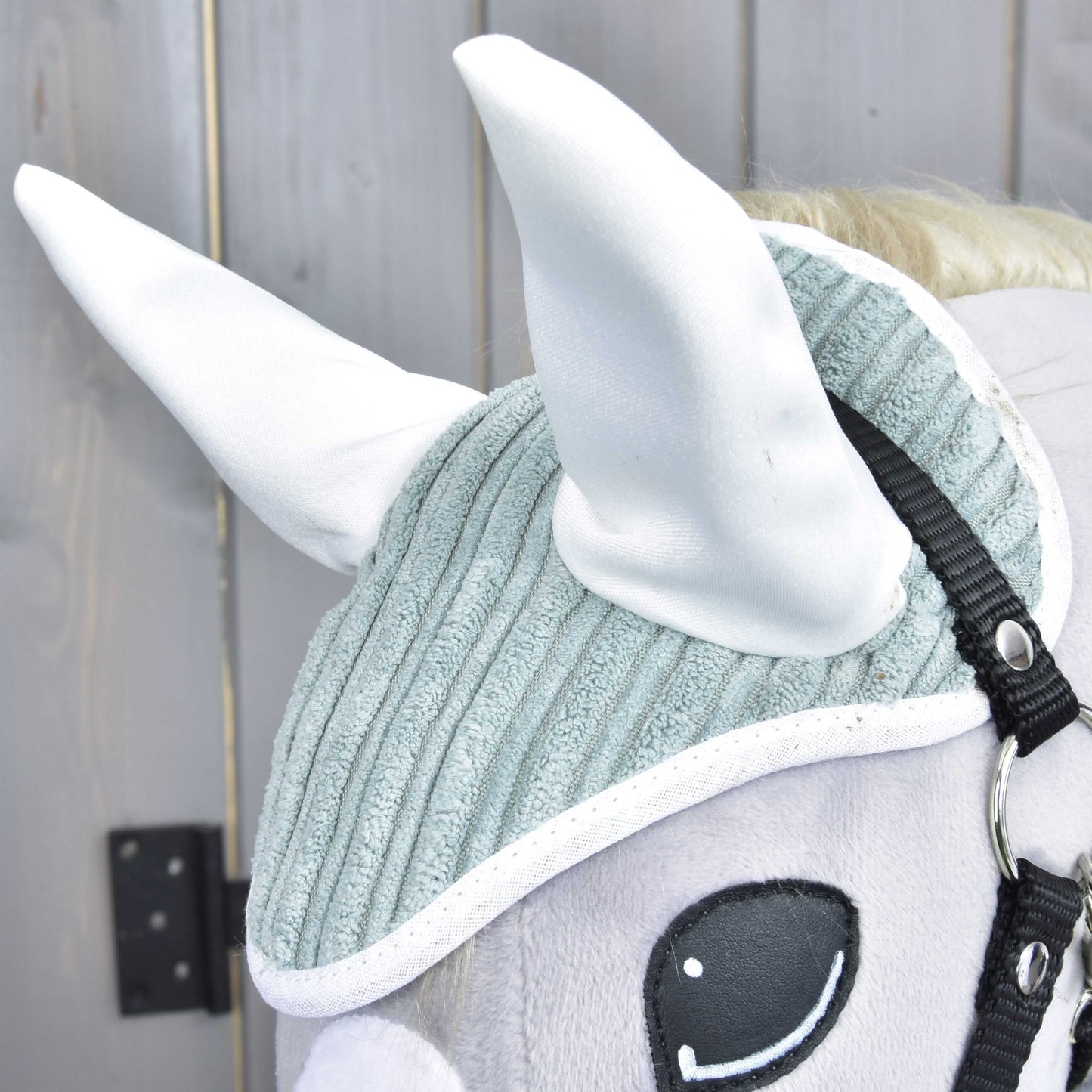 Detail Set Manchester Little Green od Hobby Horse LarDen: plyšová koňská hlava s texturovanou světle šedou čabrakou na uši, velkými bílými ušima, černou uzdečkou a vyšívaným okem na dřevěném pozadí.