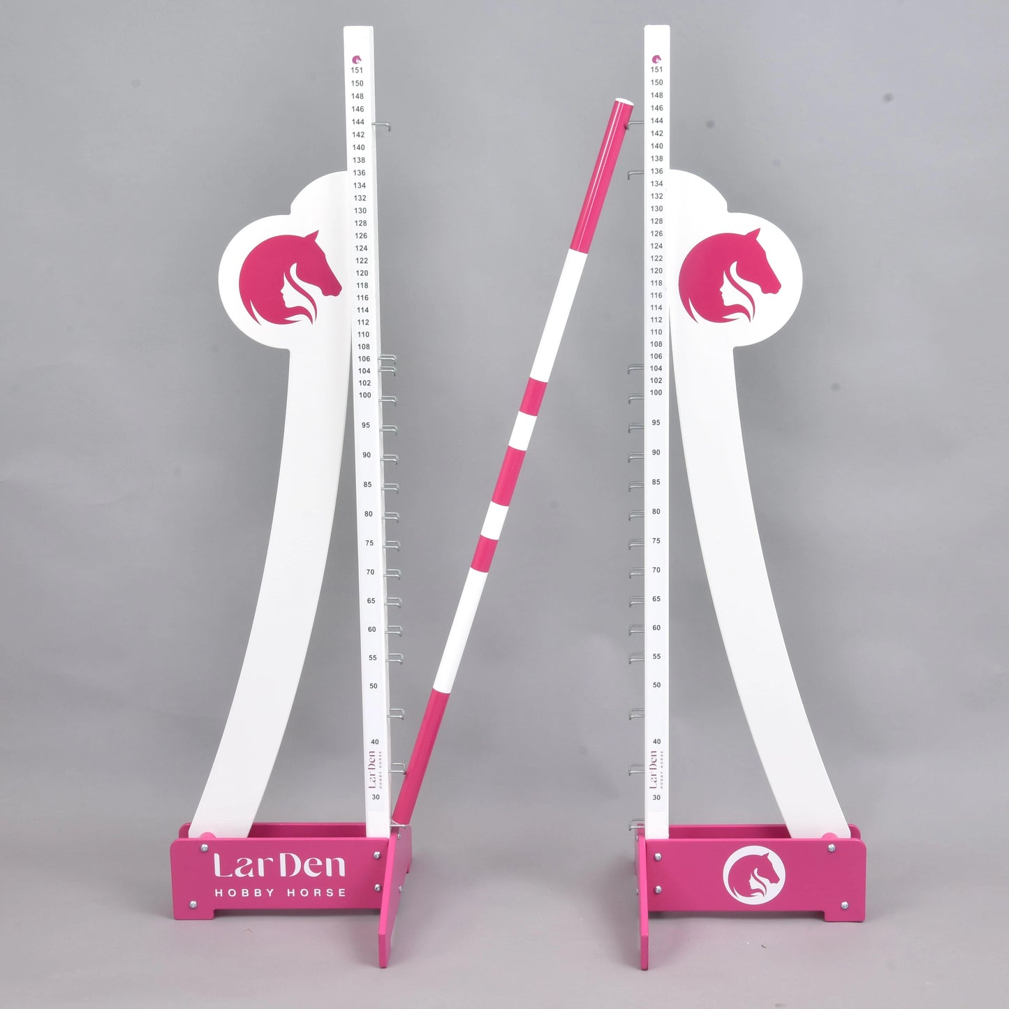 LarDen skok mohutnosti od Hobby Horse LarDen, dvě bílé a růžové nastavitelné stojky s logy koňské hlavy drží vodorovně pruhovanou tyč, na jednobarevném šedém pozadí.