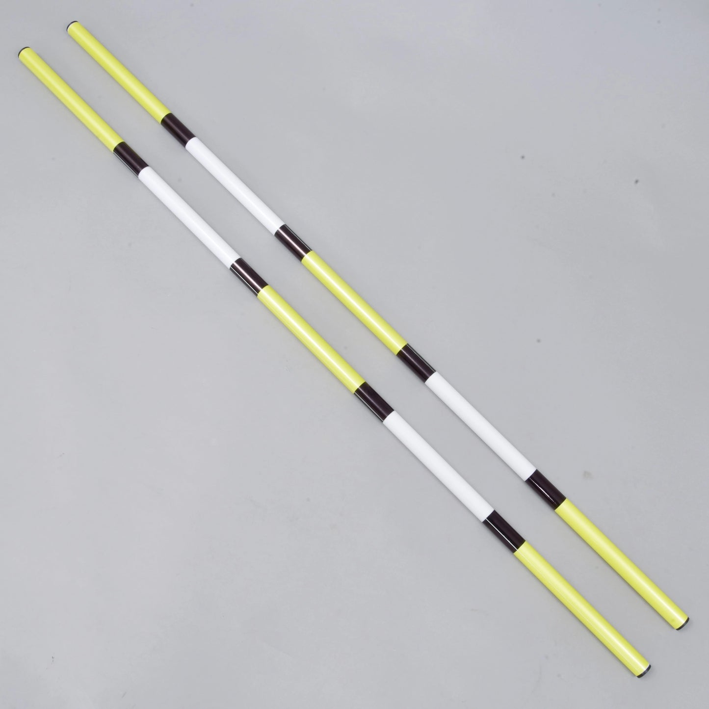 Bariérka žluto-černá, 2 ks od Hobby Horse LarDen obsahuje dvě lehké tyče z potaženého PVC o průměru 32 mm se střídajícími se žlutými, bílými a černými částmi, zobrazené rovnoběžně na světle šedém povrchu.