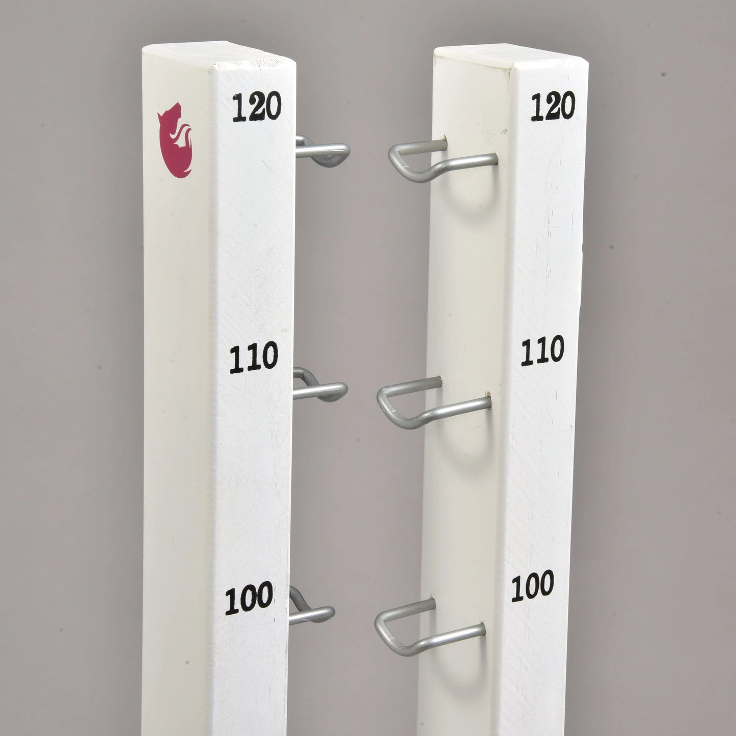 Set překážek pro Hobby Horsing od Hobby Horse LarDen se dvěma bílými svislými stojkami s kovovými držáky ve výškách 100, 110 a 120, ideální pro skoky nebo cavaletti. Levá stojka je nahoře opatřena logem červené lišky. Pozadí je jednobarevné šedé.