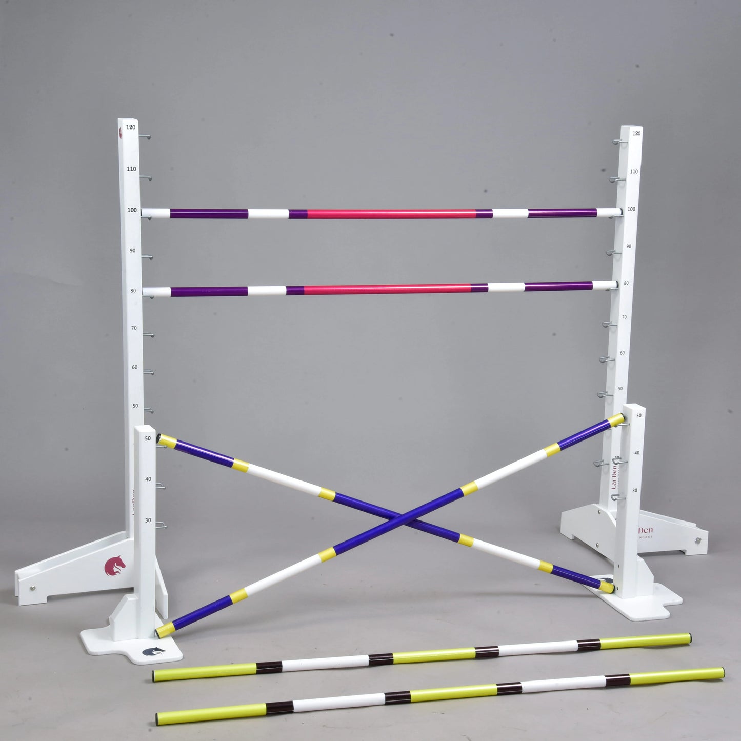 Set překážek pro Hobby Horsing od Hobby Horse LarDen zahrnuje bílé stojany s měřicími značkami, čtyři barevné tyče (dvě vodorovné a dvě zkřížené) a vpředu dvě žluto-černé cavaletti, zobrazené na jednobarevném šedém pozadí.