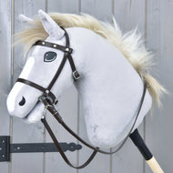 Kompletní uzdečka hnědá s kamínky z koženky od Hobby Horse LarDen na světle šedém Hobby Horse s bílou hřívou, upevněném na dřevěné tyči před šedými dřevěnými dveřmi.