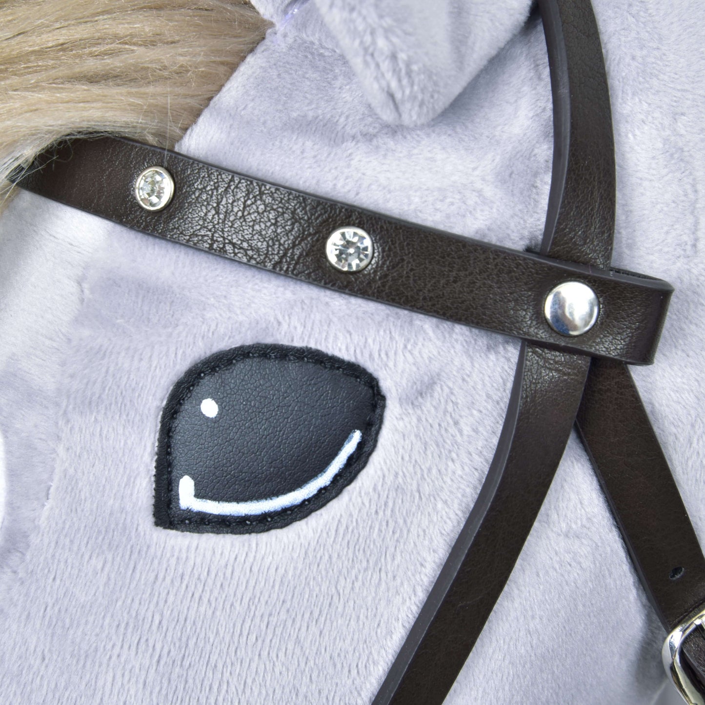 Detail obličeje plyšového koně s černobíle vyšitým okem, světle šedou srstí a kompletní uzdečkou hnědou s kamínky z koženky od Hobby Horse LarDen.