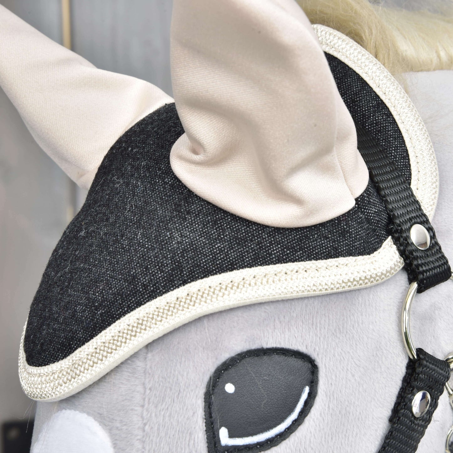 Detailní záběr na hlavu Set Blue Denim od Hobby Horse LarDen ukazuje černou uzdečku s bílým lemováním, krémové uši, hladký šedý povrch a vyšívané oko – roztomilá dekorace pro milovníky koní.