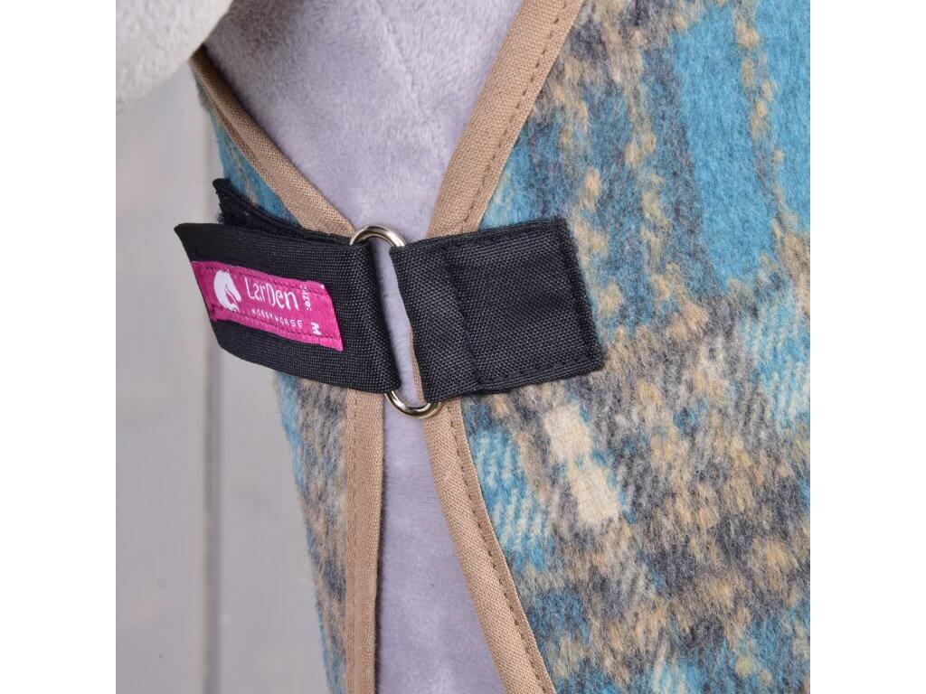 Detail deky Deka stájová Scottish Cube od Hobby Horse LarDen s modrými, hnědými a šedými vzory a béžovým lemem. Je upevněná černým popruhem se stříbrným kroužkem a doplněná růžovým štítkem s logem koně.