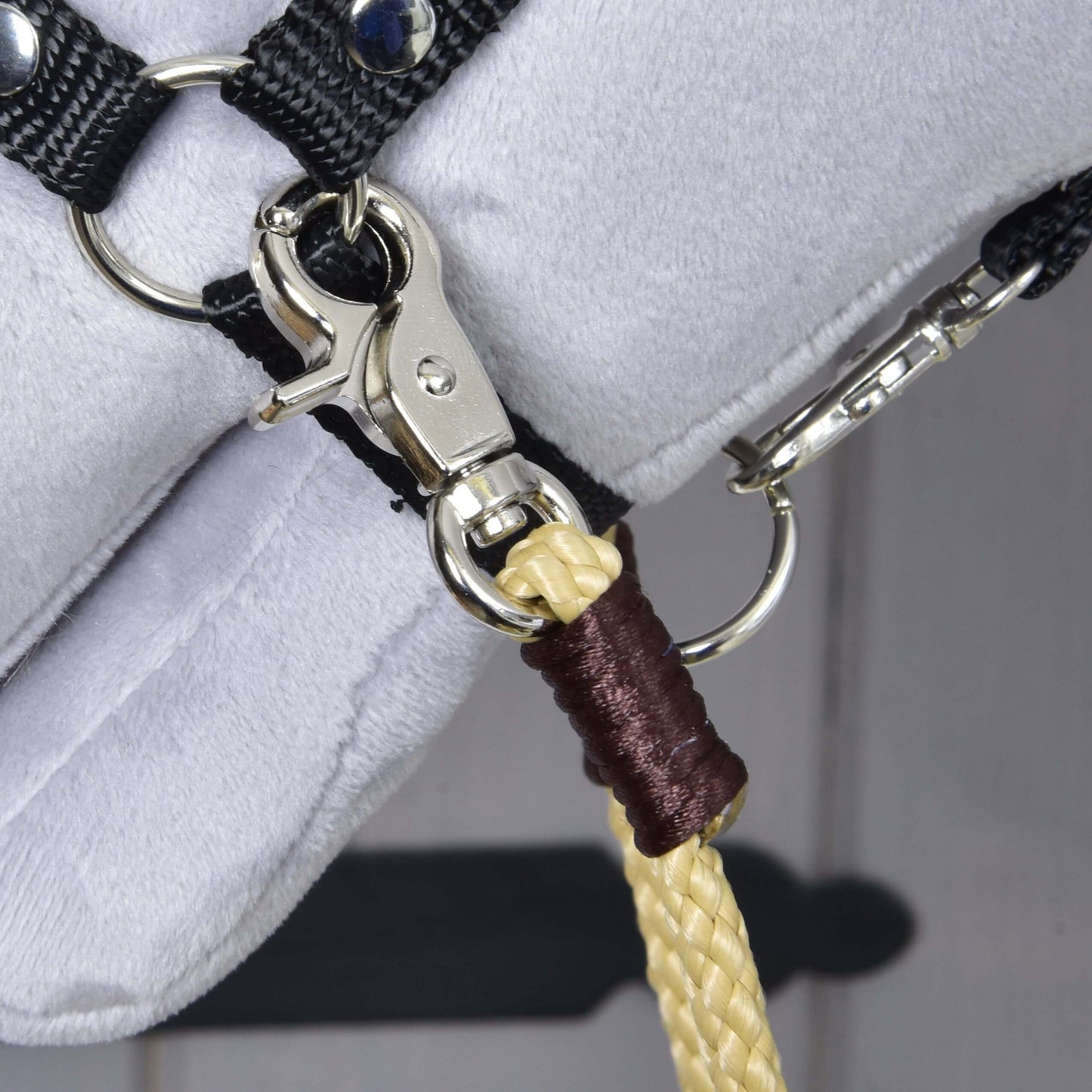 Detail kovové karabiny na černém řemínku s pleteným žlutým lanem upevněným hnědou nití – ideální pro trénink s Westernovými otěžemi Dakota od Hobby Horse LarDen na bílém povrchu.