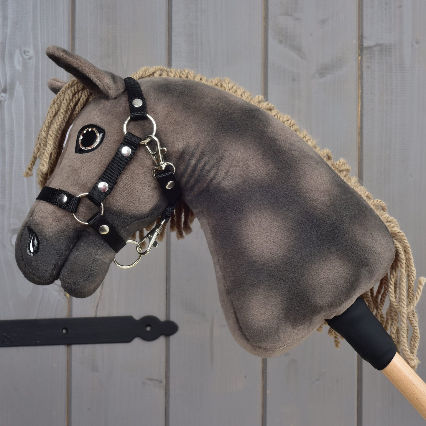 Hobby Horse Avalon s černou ohlávkou, velikost XS, od Hobby Horse LarDen, s plyšovým provedením na dřevěné tyči ve stylu elegantního sportovního koně plemene English Warmblood, na šedém dřevěném pozadí.