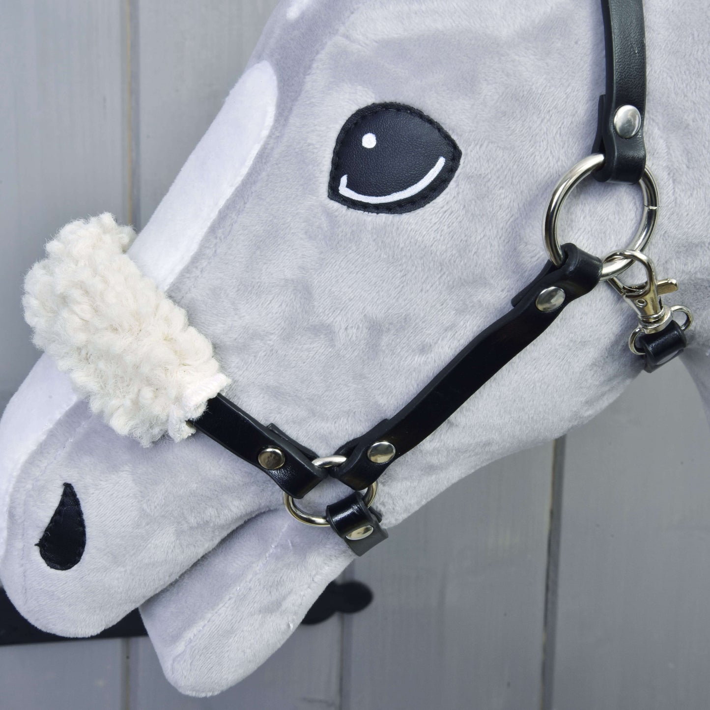 Detail šedé hlavy Set Basic Hobby Horse od Hobby Horse LarDen s černou uzdečkou s otěžemi a bílým chlupatým nánosníkem na světlém dřevěném pozadí.