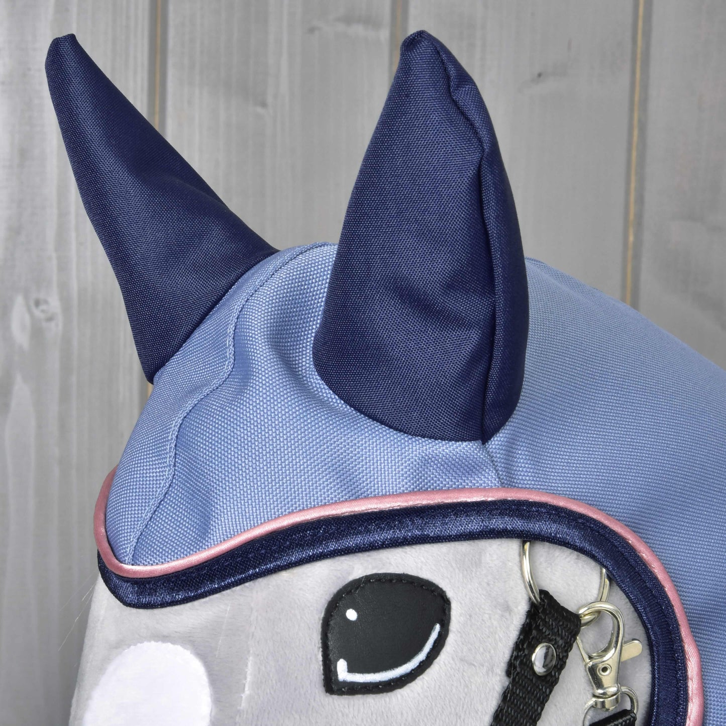 Detail Pláštěnky Bloom od Hobby Horse LarDen, plyšové koňské hračky se světle modrou a tmavě modrou čabrakou s velkými tmavě modrými ušima a detailním prošíváním. Ideální pro prezentaci doplňků pro hobby horse na dřevěném pozadí.