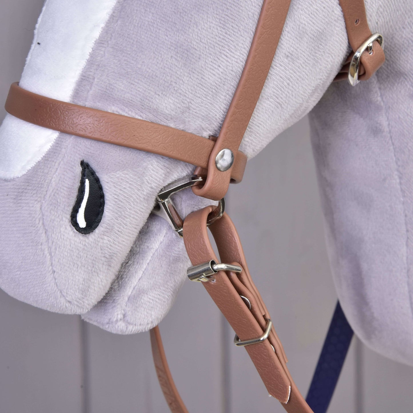 Detail plyšové koňské hlavy Hobby Horse LarDen s Kompletní uzdečka s nánosníkem Brown Purple a vyšívaným černo-bílým okem ve tvaru kapky.