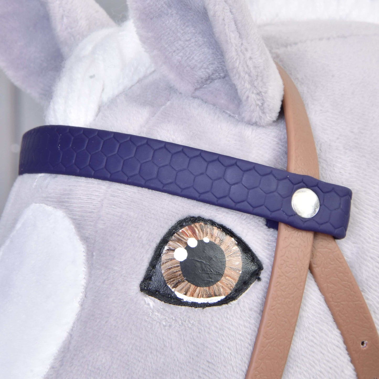 Detail hračky Hobby Horse LarDen s Kompletní uzdečka s nánosníkem Brown Purple: propracované látkové oko, tmavě fialová uzdečka z koženky, béžový řemínek a jemná světle šedá srst.