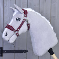 Ohlávka s beránkem z koženky Burgundy od Hobby Horse LarDen na šedém plyšovém Hobby Horse s bílou hřívou a vínovou uzdečkou dodává stylový vzhled na pozadí šedé dřevěné stěny — je tak dokonalým doplňkem.