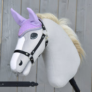 Plyšový Hobby Horse se světle šedým tělem, černou uzdečkou a krémovou hřívou nosí Čabraka Orchid od Hobby Horse LarDen pro ochranu před hmyzem. V pozadí je dřevěný plot.