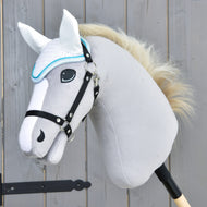 Detail šedého plyšového Hobby Horse od Hobby Horse LarDen s bílou hřívou, černou uzdečkou a čabrakou háčkovanou Glitter Cuties pro ochranu proti mouchám, nasazeného na dřevěné tyči před dřevěným plotem.