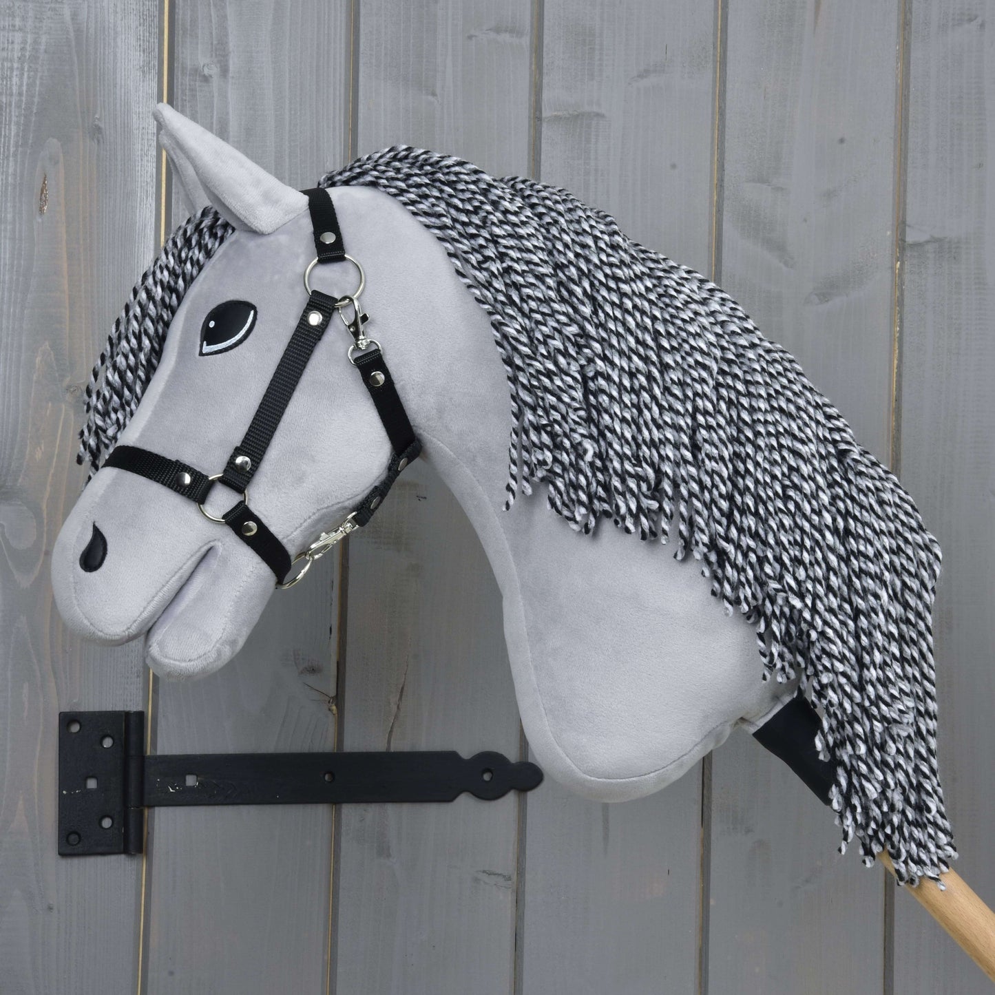 Hobby Horse Caesar s černou ohlávkou od Hobby Horse LarDen, se šedou plyšovou hlavou, černobílou přízovou hřívou, černou ohlávkou a velkýma kreslenýma očima na dřevěné tyči – ideální pro nápaditou hru.