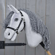 Hobby Horse Caesar s černou ohlávkou od Hobby Horse LarDen, se šedým plyšovým tělem, černobílou přízovou hřívou a černou ohlávkou, zobrazený na dřevěné tyči na pozadí dřevěného plotu.