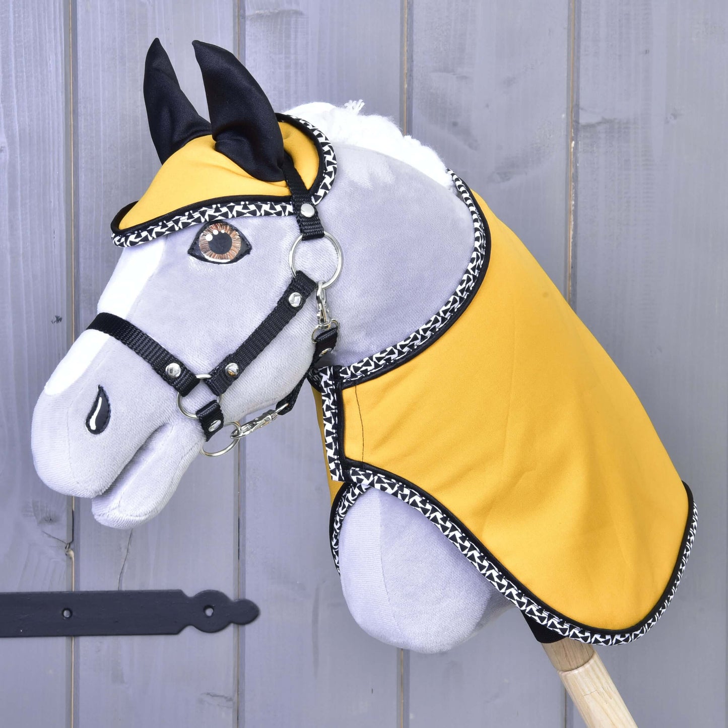 Set Yellow Beauty od Hobby Horse LarDen tvoří plyšový Hobby Horse se šedým obličejem, černou uzdečkou, žlutým látkovým potahem s černobílým lemováním a ladící dekou, zobrazený na dřevěném pozadí.