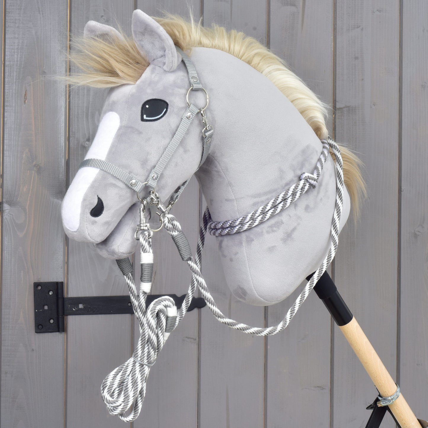 Set Start stříbrný (ohlávka + nákrčník + vodítko + otěže) od Hobby Horse LarDen na šedém plyšovém Hobby Horse s bílým pruhem na hlavě, nasazeném na dřevěné tyči a opřeném o šedou dřevěnou stěnu.