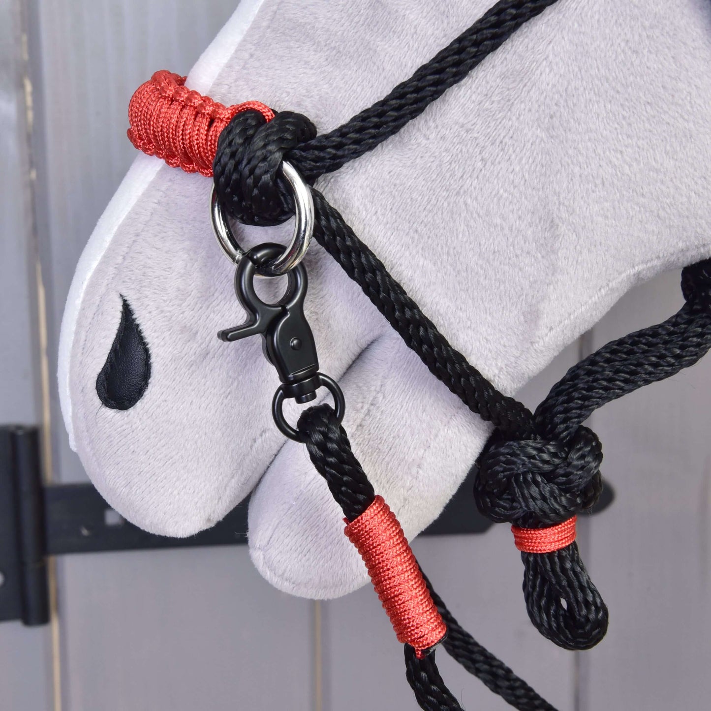 Detail hlavy bílého plyšového koně s ohlávkou Hobby Horse LarDen Provazový set Spark s červeným omotáním a kovovou karabinou, s černým znakem ve tvaru slzy u oka.