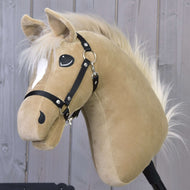 Hobby Horse Dancing Lady s černou ohlávkou od Hobby Horse LarDen, béžová plyšová klisna s bílou hřívou a bílou lysinou, stojí před stěnou z dřevěných prken.