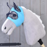 Plyšový Hobby Horse se světle šedým tělem, bílou hřívou a modrou pratelnou Maska proti hmyzu od Hobby Horse LarDen, nasazený na dřevěné tyči na pozadí šedého dřeva.