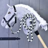 Hobby Horse - pletené vodítko černá/bílá od Hobby Horse LarDen na šedé plyšové hlavě Hobby Horse s bílou hřívou, černou uzdečkou a přiloženým černobílým pleteným vodítkem, zobrazené před šedým dřevěným pozadím.