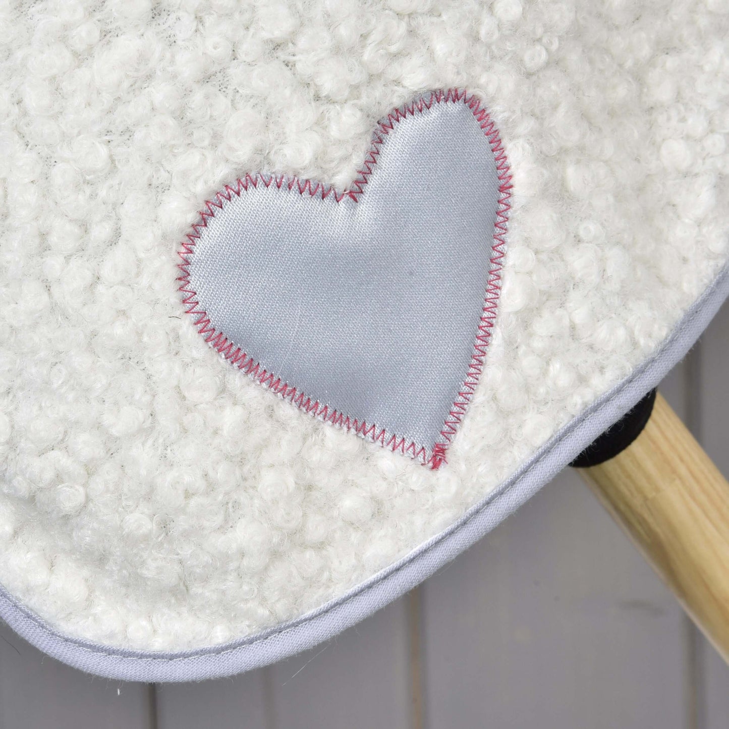 Detail bílé texturované čabraky Set Snowflake od Hobby Horse LarDen s lesklou světle šedou nášivkou ve tvaru srdce a růžovým cikcak stehem; v pravém dolním rohu je vidět dřevěná tyč.