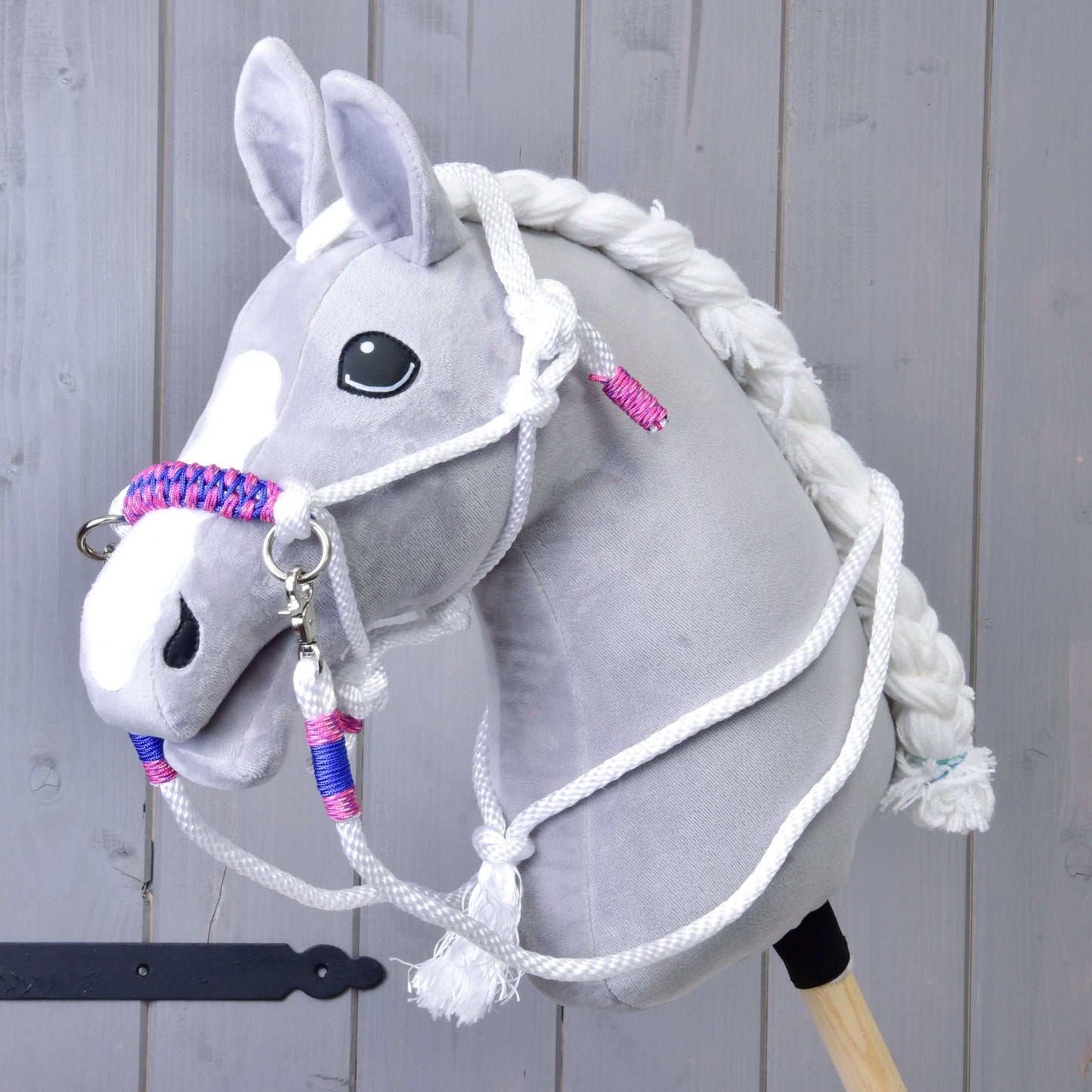 Provazový set Bílý (vel. M) od Hobby Horse LarDen na šedém plyšovém Hobby Horse s bílou hřívou, otěžemi a pletenou ohlávkou s růžovými a modrými akcenty, na dřevěném pozadí.
