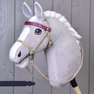 Hobby Horse LarDen se šedým Hobby Horse s bílou hřívou, černým okem a koženkovým setem Bordeaux – uzdečka, otěže a martingal –, doplněným o fialovou čelenku a obličej v kresleném stylu. Stojí vzpřímeně před dřevěným pozadím.