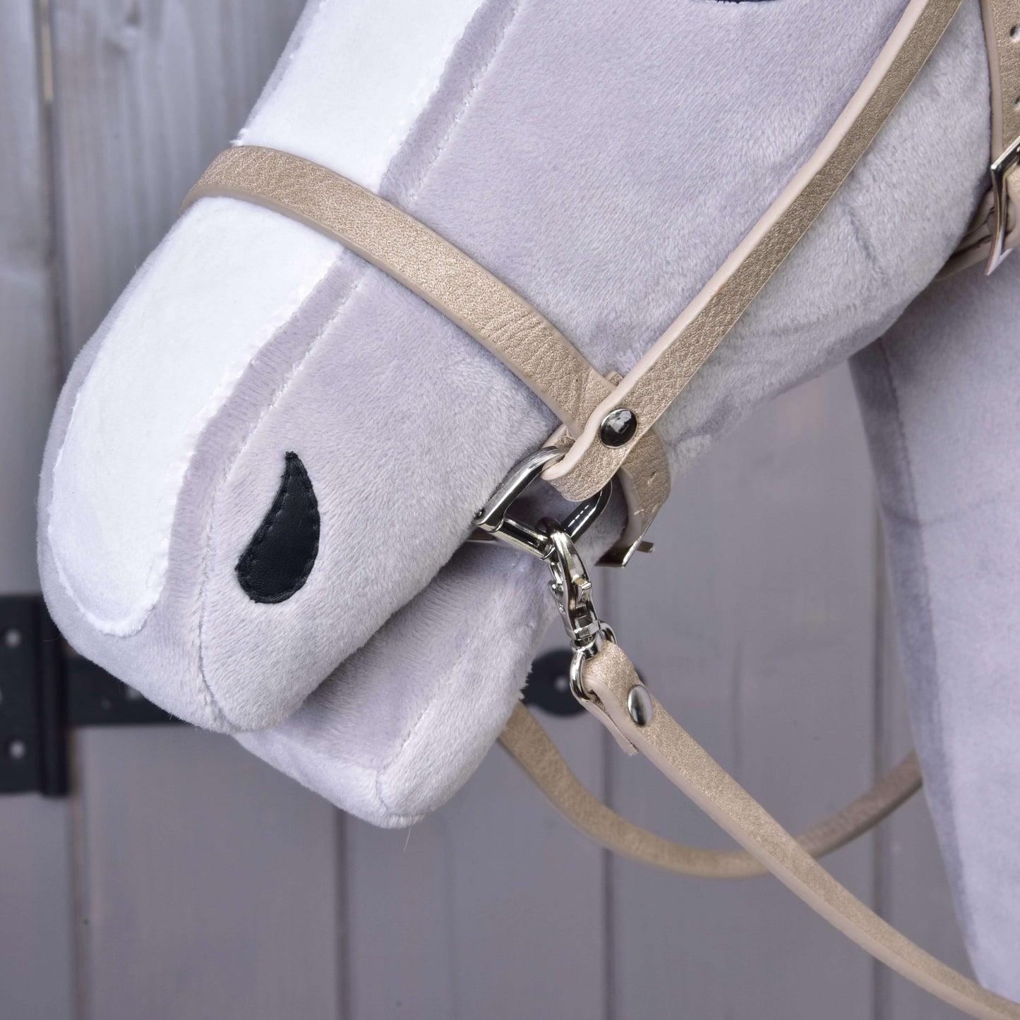 Detail hlavy plyšového koně Hobby Horse LarDen s koženkovým setem Bordeaux – uzdečka, otěže a martingal – a s černě prošitou nozdrou a tlamou, zobrazený před dřevěným pozadím.