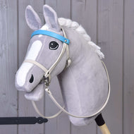 Hobby Horse LarDen se šedým plyšovým Hobby Horse s výraznýma očima, bílou hřívou a koženkovým setem Aqua – uzdečka, otěže a martingal –, upevněným na dřevěné tyči před pozadím ze světle šedých dřevěných panelů.