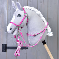 Plyšový šedý Hobby Horse LarDen s bílou hřívou je zobrazen se sadou Set Start Růžový (ohlávka + nákrčník + vodítko + otěže), upevněný na dřevěné tyči na pozadí šedé dřevěné stěny.