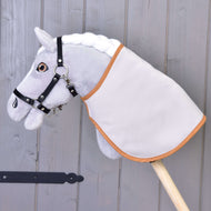 Šedý Hobby Horse LarDen s bílou hřívou, černou uzdečkou a Dekou anglická kostka, hnědá a oboustranná, nasazený na dřevěné tyči před šedou dřevěnou stěnou.