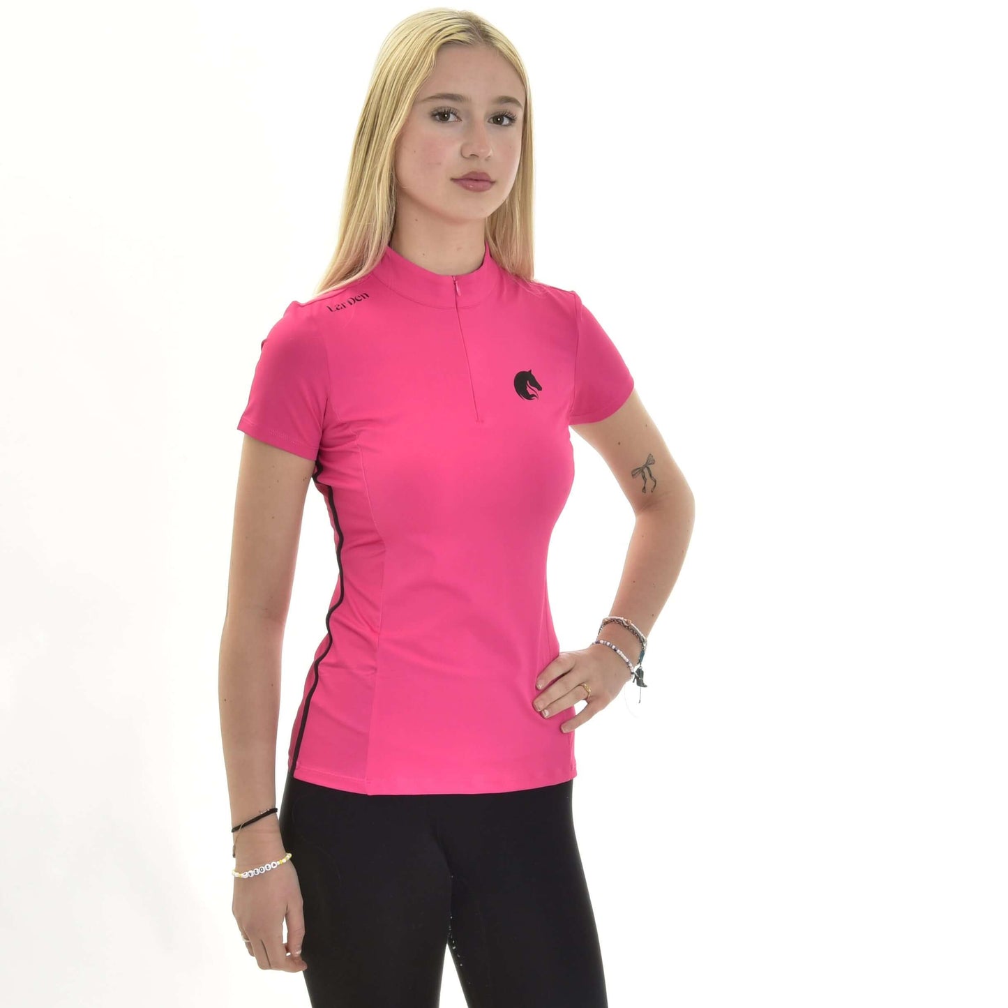 Sportovní triko LarDen Pink od Hobby Horse LarDen, zářivě růžový sportovní top s krátkým rukávem ze spandexu, předvádí mladá žena s dlouhými blond vlasy, v kombinaci s černými kalhotami, pózující na čistě bílém pozadí s jednou rukou v pase.