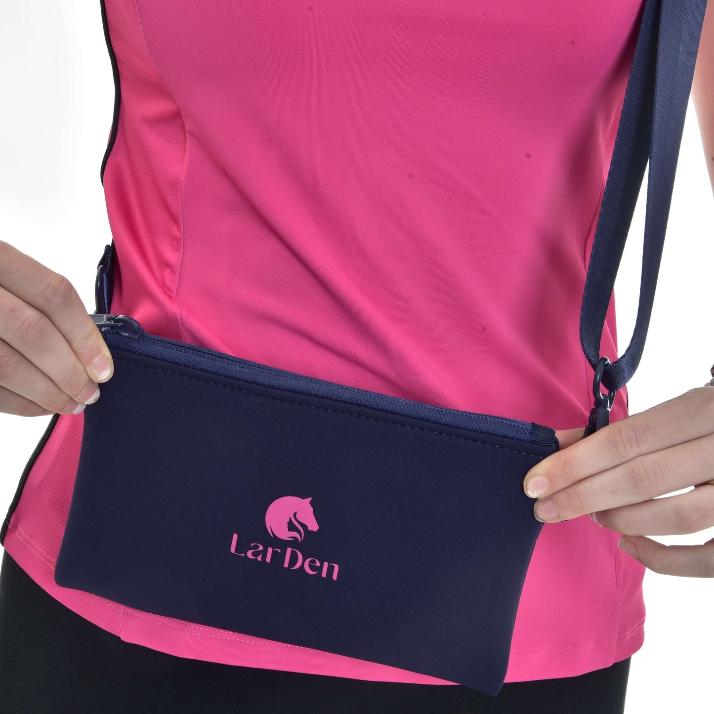 Osoba v růžovém sportovním topu drží Hobby Horse LarDen Crossbody, tmavě modrou neoprenovou tašku s nastavitelným popruhem, zapínáním na zip a logem značky s grafikou koně.