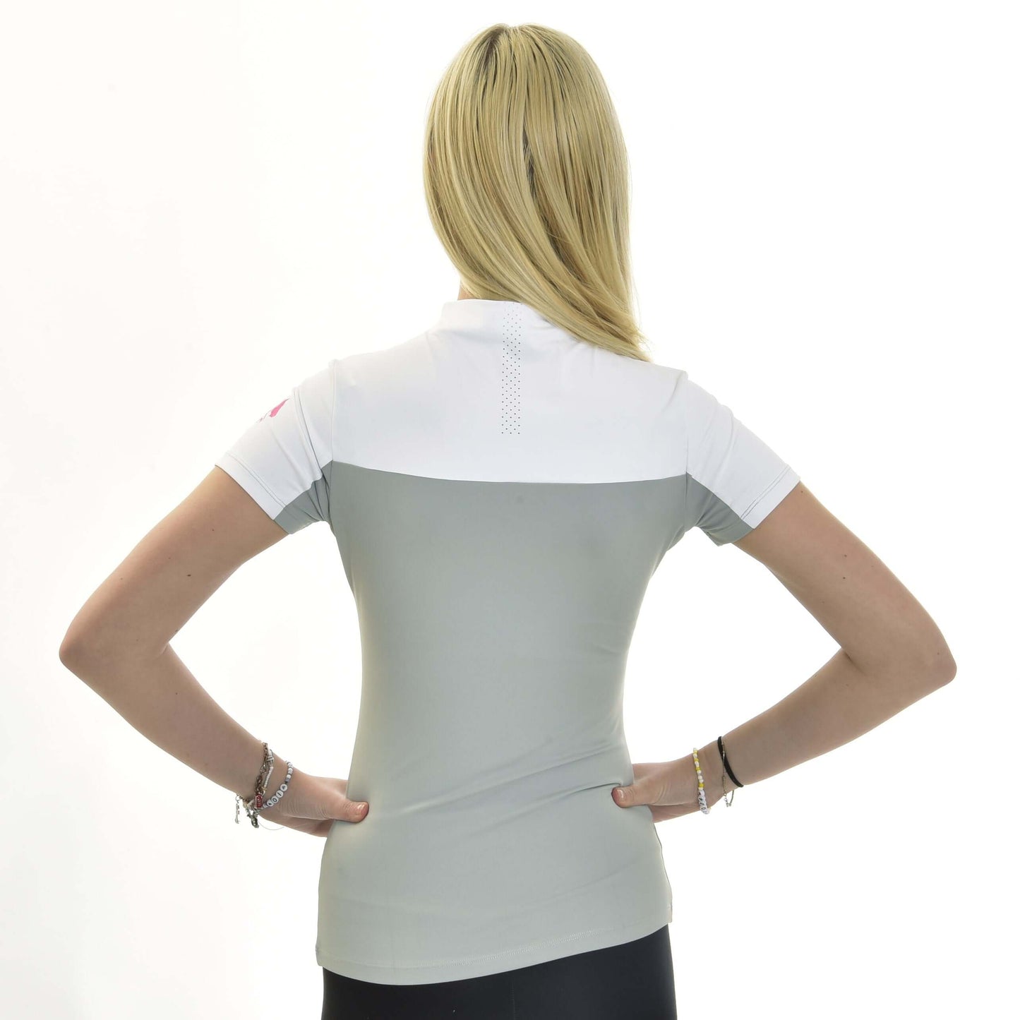 Žena s dlouhými blond vlasy stojí zády k fotoaparátu, ruce v bok, a má na sobě Sportovní triko LarDen Premium od Hobby Horse LarDen v bílé a světle šedé barvě ze spandexu. Pozadí je čistě bílé.