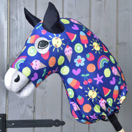 Látková hlava Hobby Horse s černýma ušima, velkýma očima a modrým ochranným oblekem Hobby Horse Happiness od Hobby Horse LarDen se slunci, duhami, srdíčky, ovocem a zmrzlinou, na dřevěném pozadí.